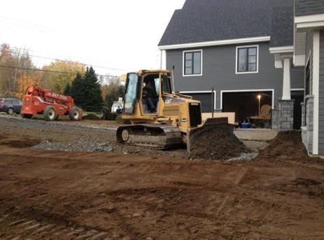 Un bulldozer déplace de la terre devant une maison