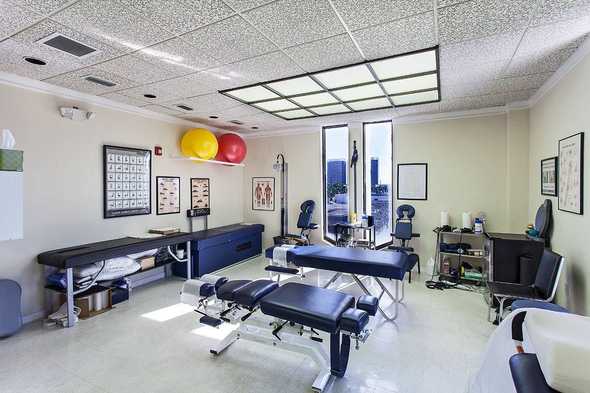 Chiropractic clinic interior with therapy tables, exercise balls, and cityscape view.