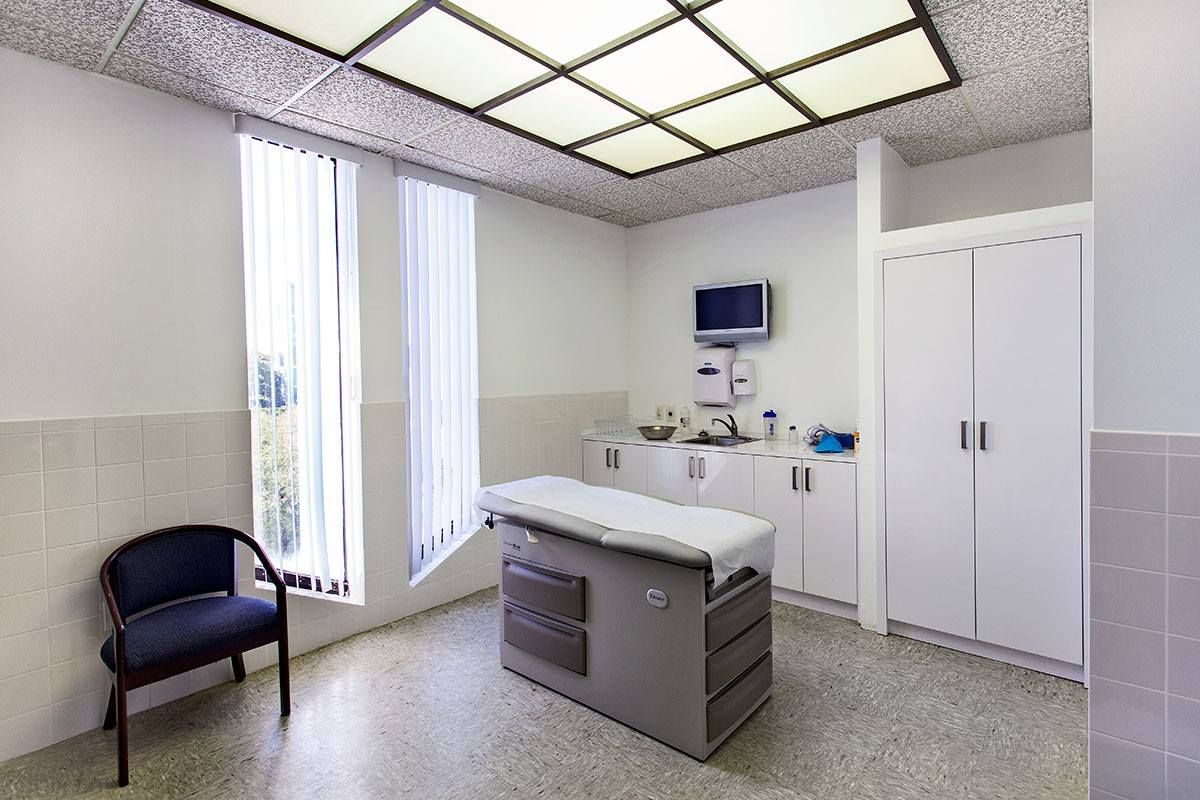 Examination room with a patient bed, medical equipment, a window with curtains, and a blue chair.