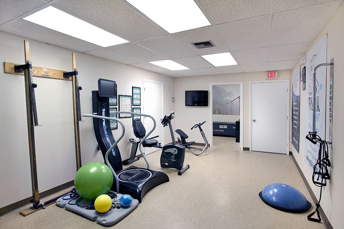 Physical therapy room with exercise equipment: machines, balance ball, and resistance bands.