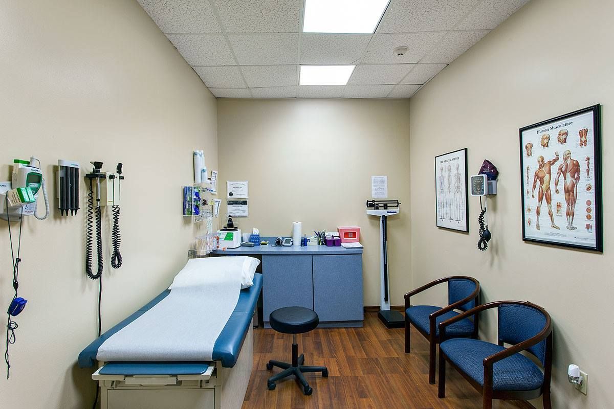 Doctor's office exam room with examination table, equipment, scale, and chairs.