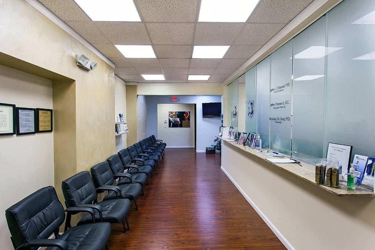 Waiting room with rows of black chairs, wood flooring, and reception desk.