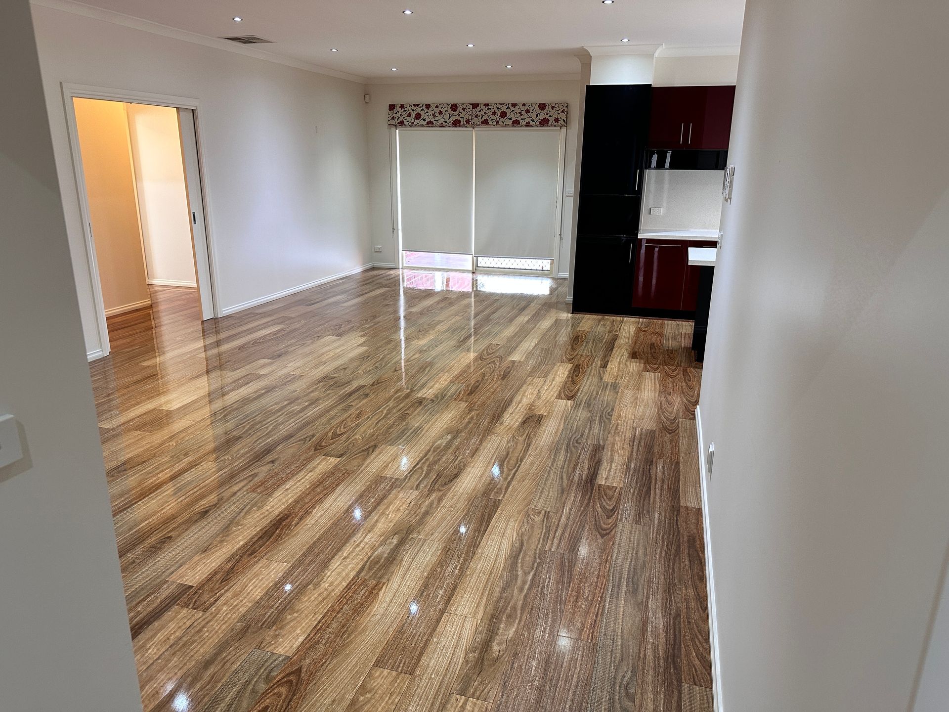 A living room with hardwood floors and a kitchen in the background.