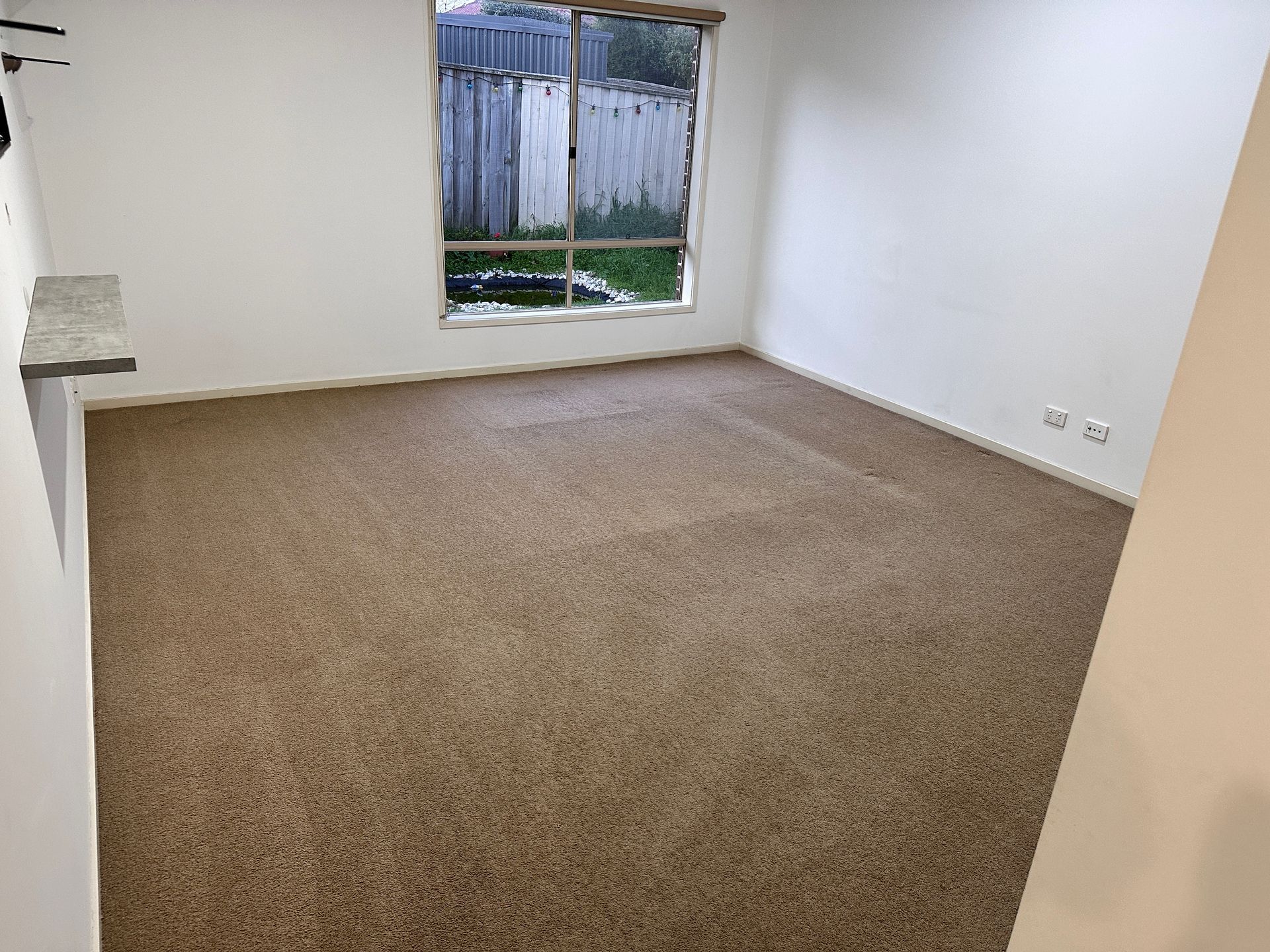 An empty room with a brown carpet and a window.