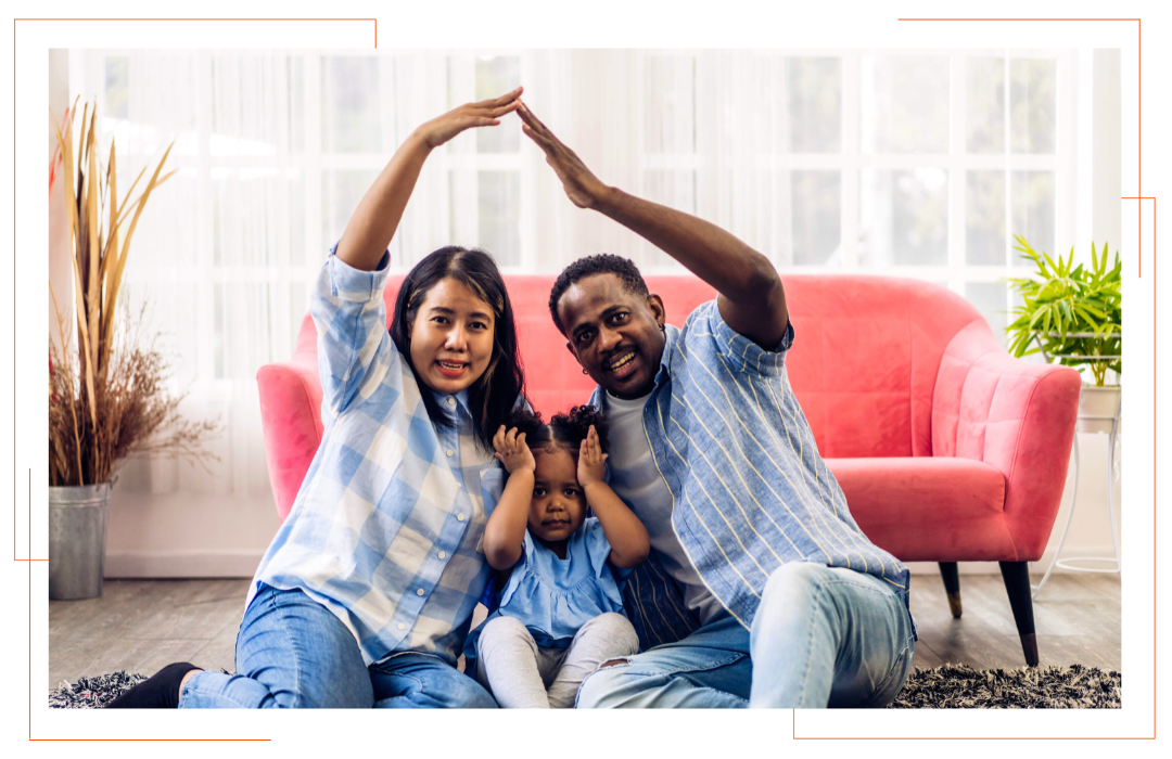 A family is sitting on the floor in a living room making a roof with their hands.