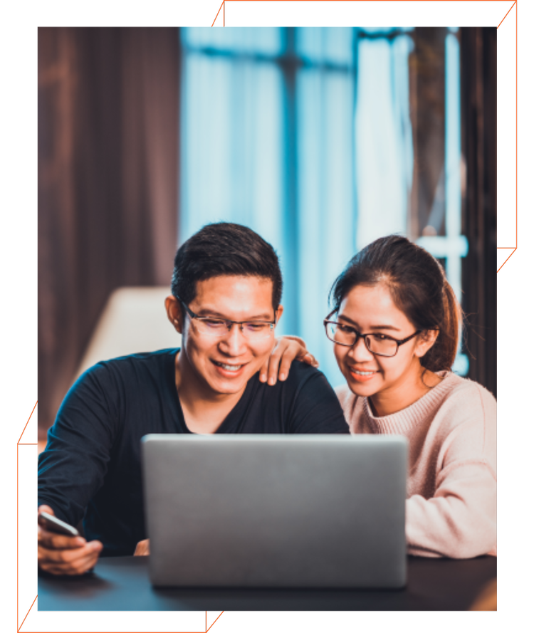 A man and a woman are sitting at a table looking at a laptop.