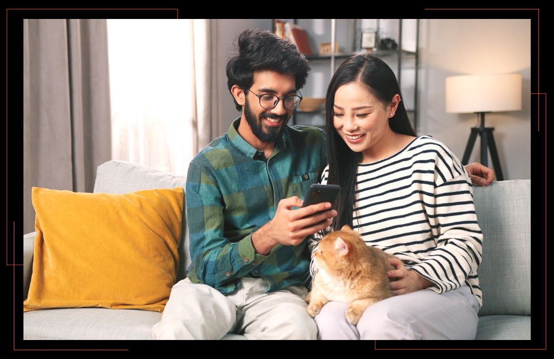 A man and a woman are sitting on a couch looking at a cell phone.