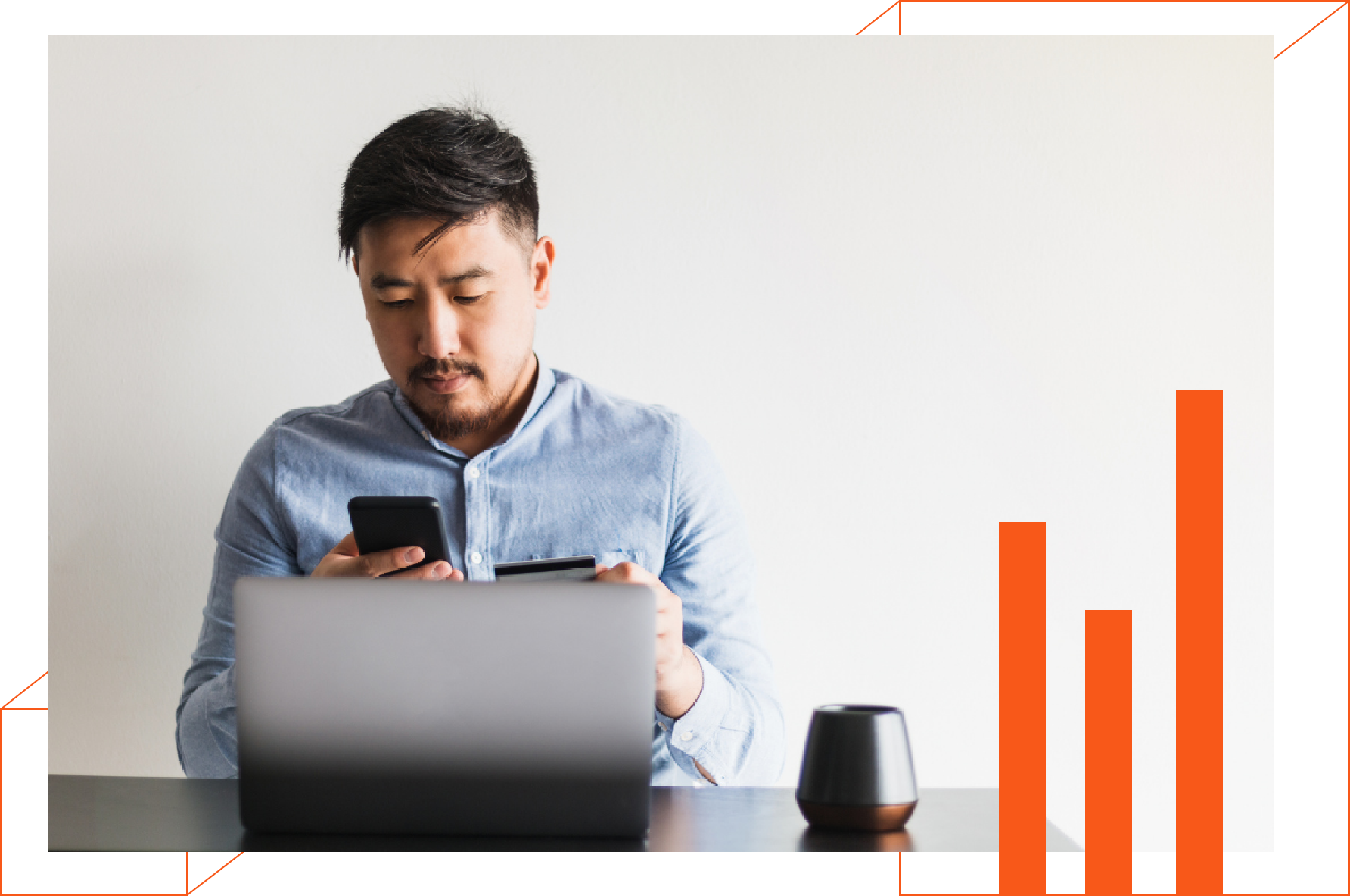 A man is sitting at a desk using a laptop and a cell phone.