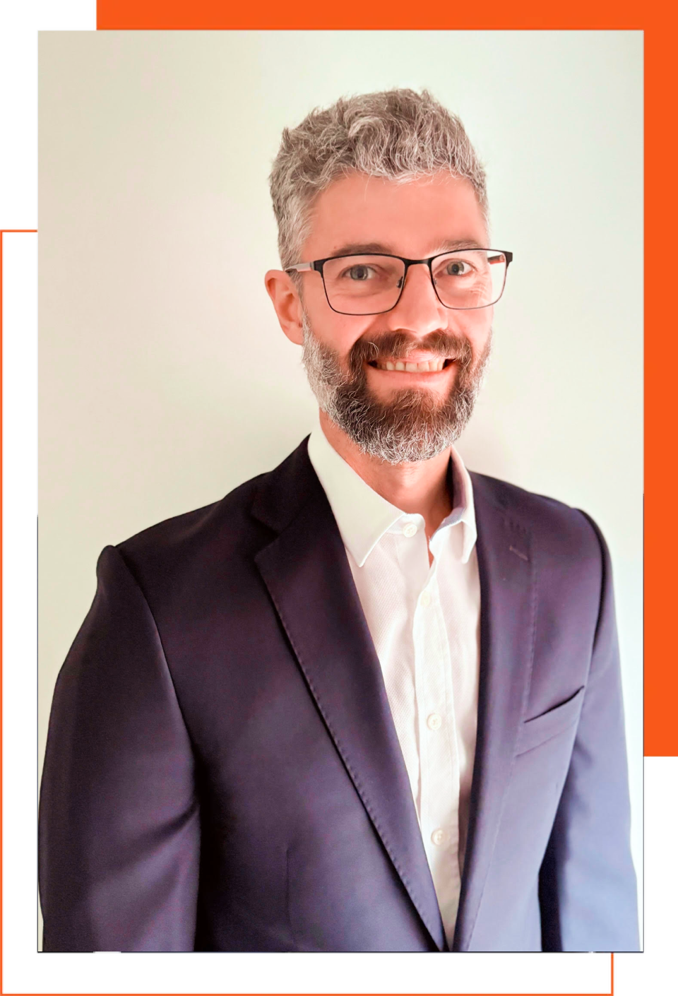 A man with a beard and glasses is wearing a suit and smiling.