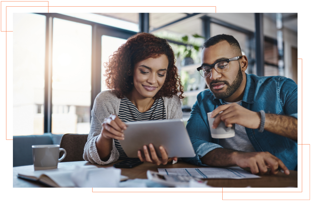A man and a woman are sitting at a table looking at a tablet.