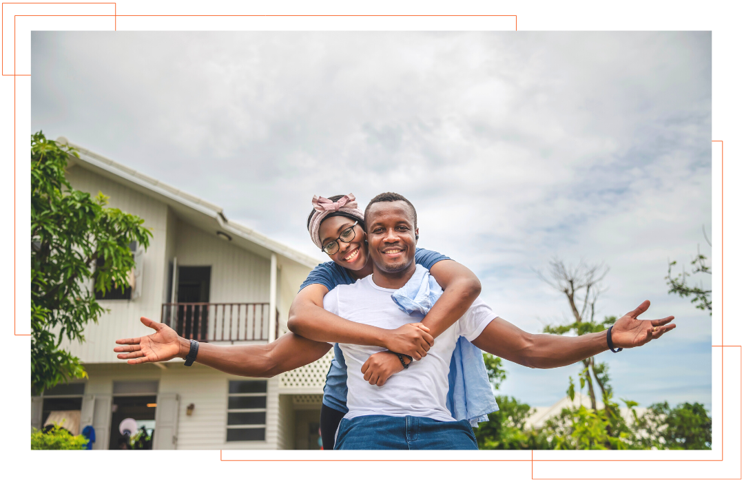 A man is carrying a woman on his back in front of a house.