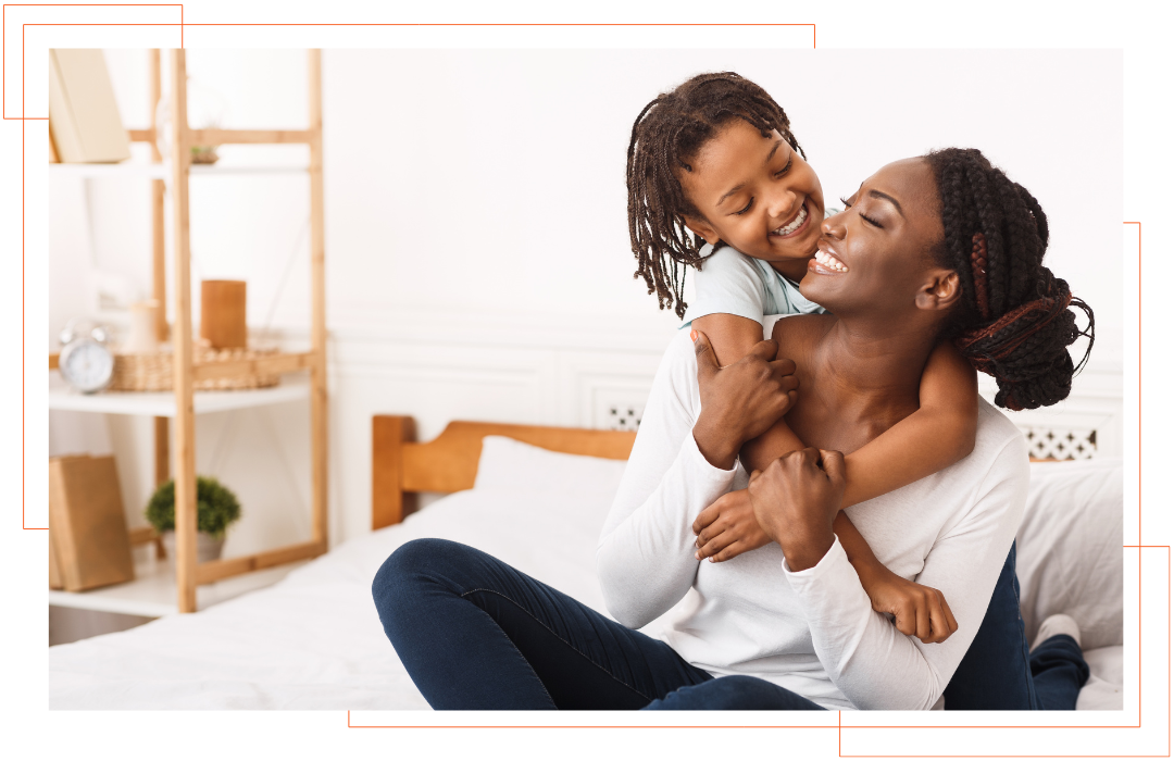 A woman is sitting on a bed holding a little girl on her shoulders.