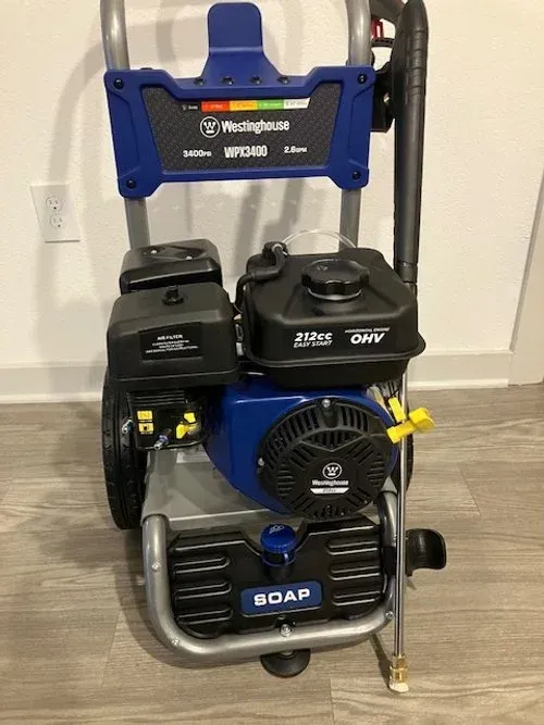 A blue and silver Westinghouse gas pressure washer with a black engine and handle on a wood floor.