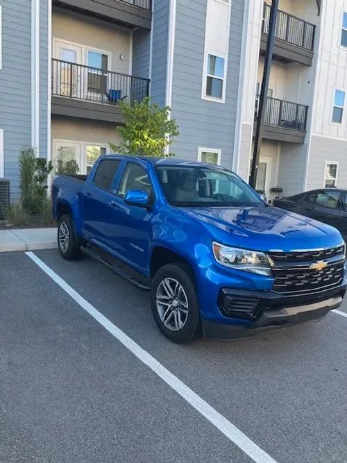 Blue Chevrolet Colorado truck parked in front of a modern apartment building.