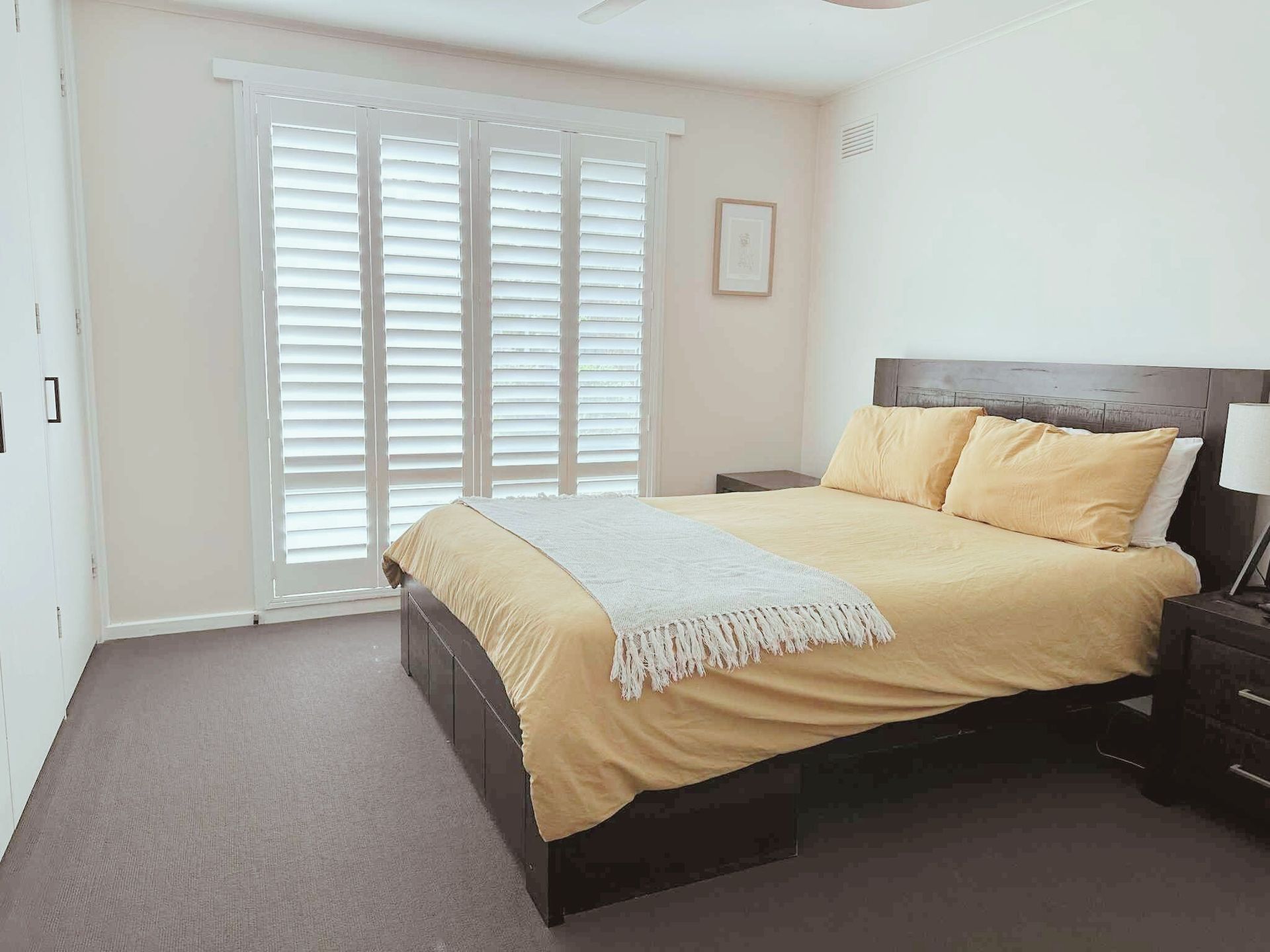Bright white bathroom with wooden vanity, window with shutters, and marble tile floor.
