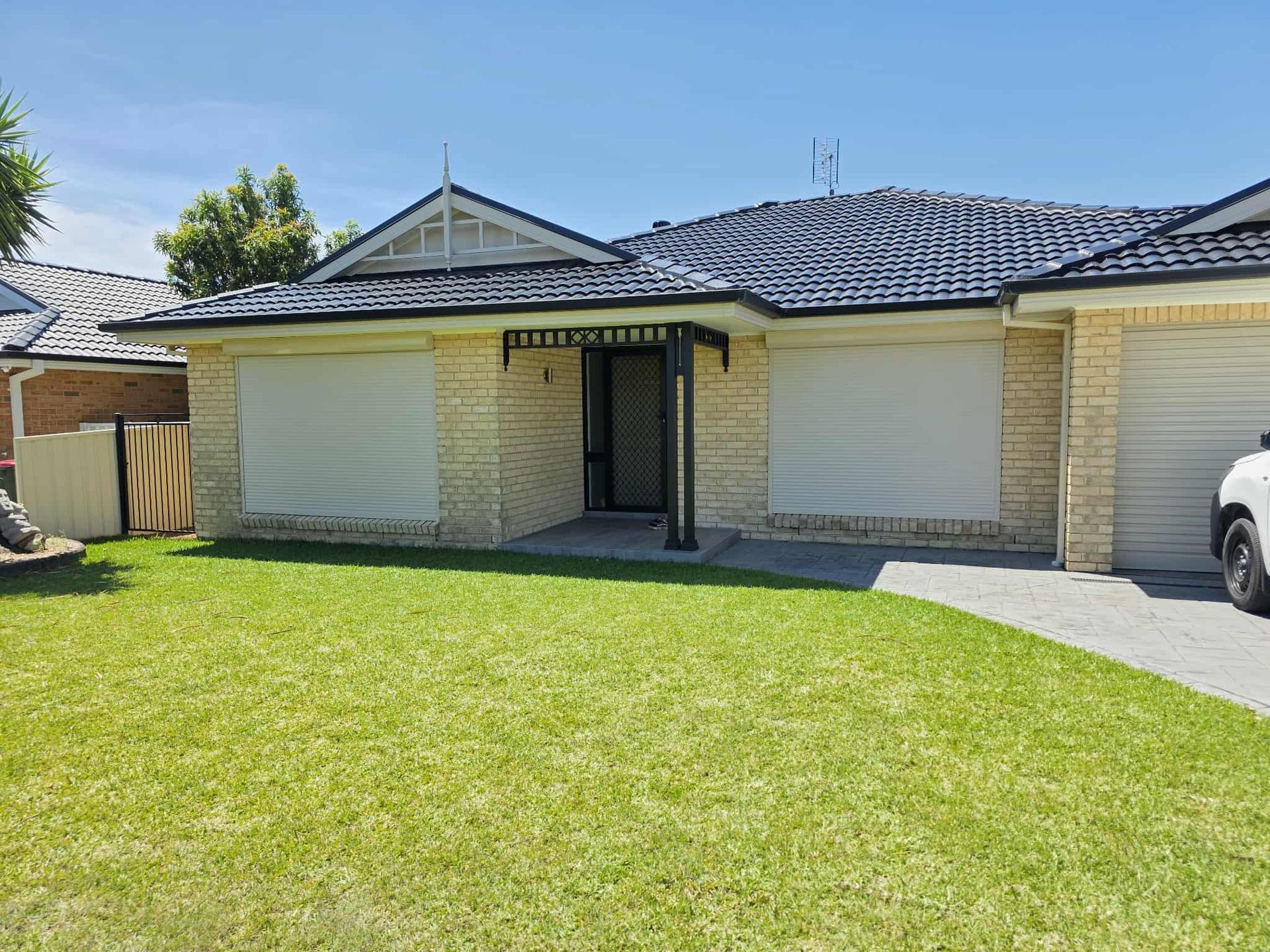 Two windows with dark gray roller shades; one shade is partially down. Sunlight reflects off the glass.