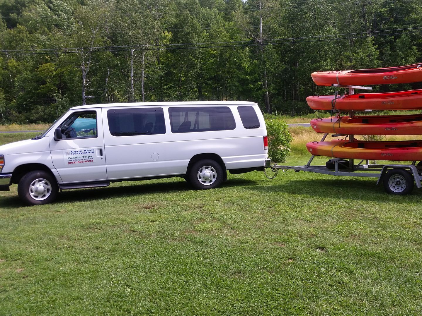 A white van is towing a trailer with kayaks on it.