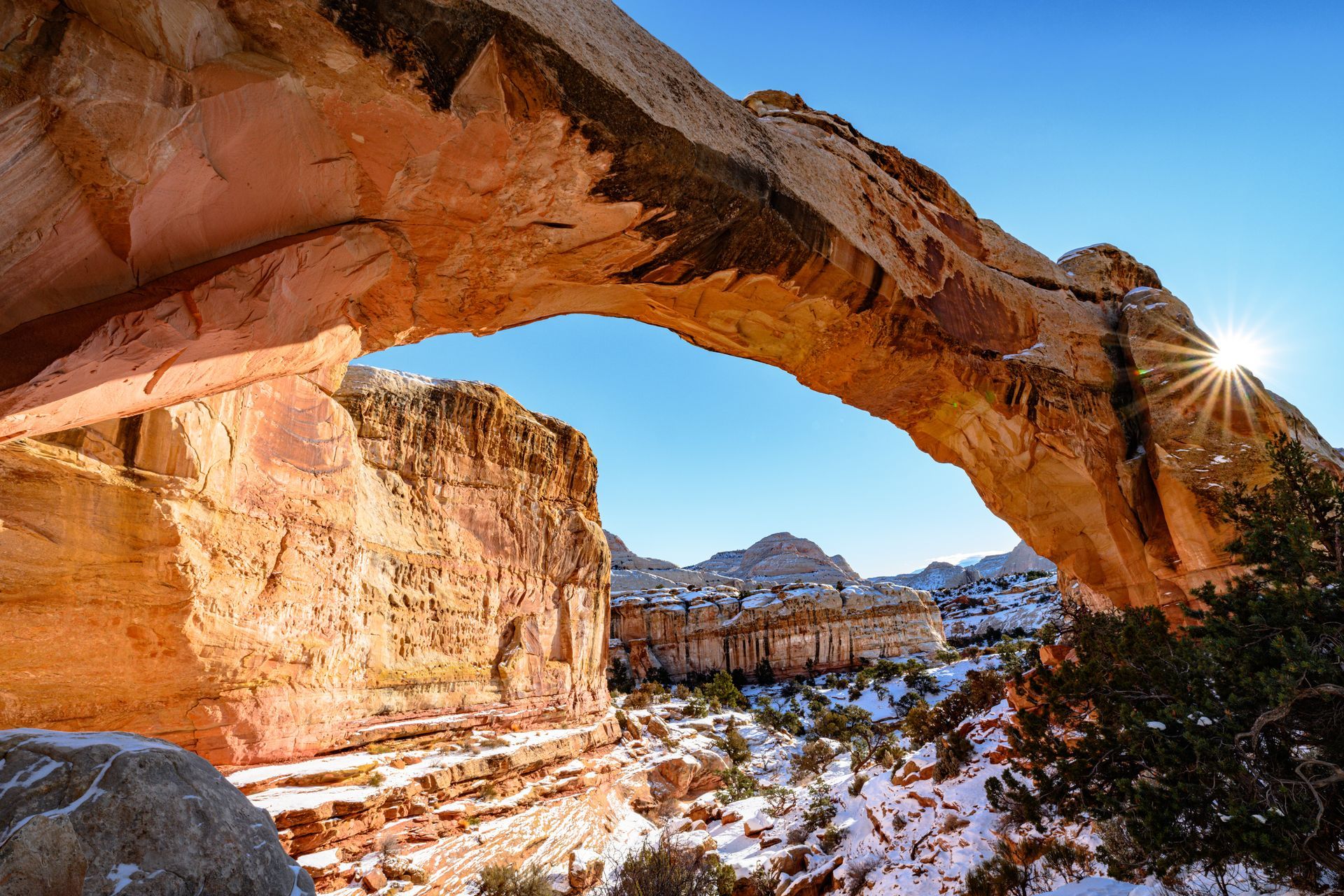 A large rock arch in the desert with the sun shining through it