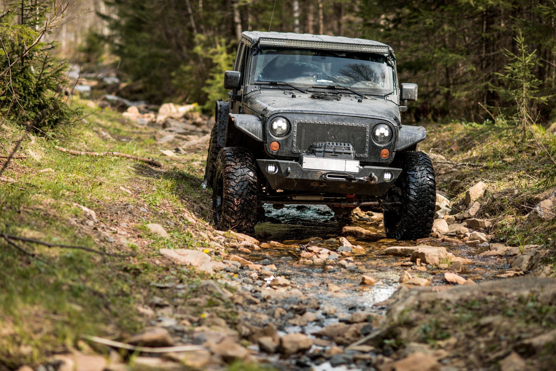 A jeep is driving down a rocky road in the woods.