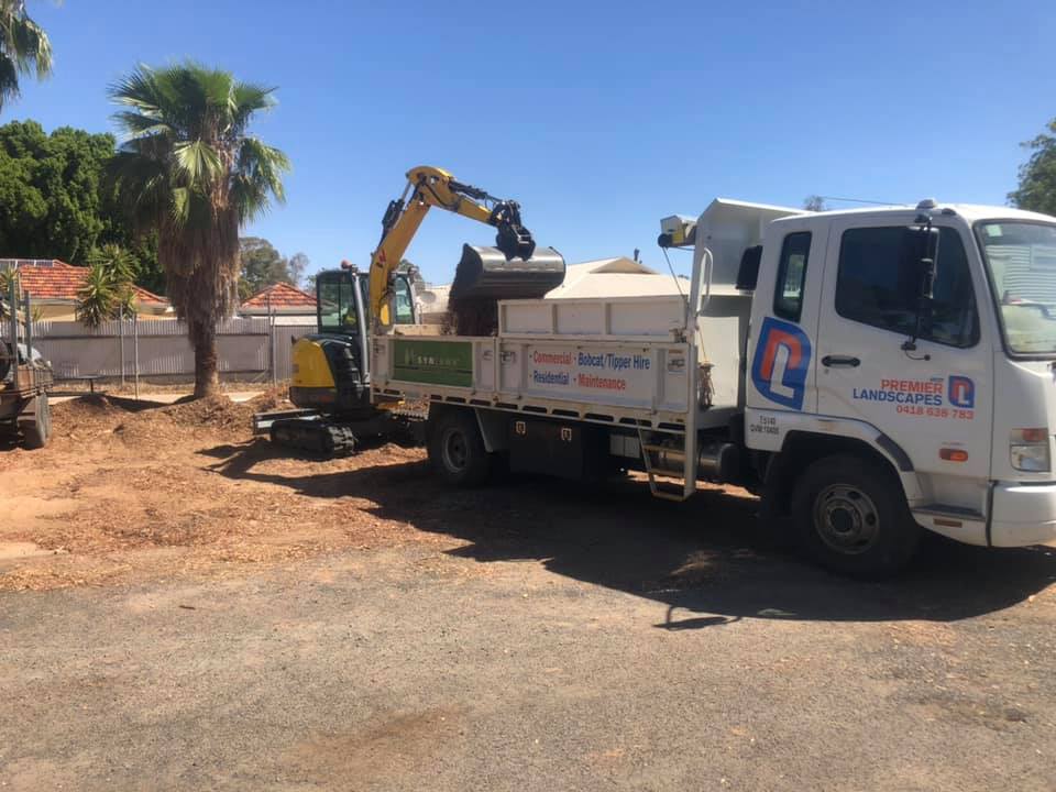 Dubbo Premier Landscape's branded truck and excavator are parked in front of a commercial area