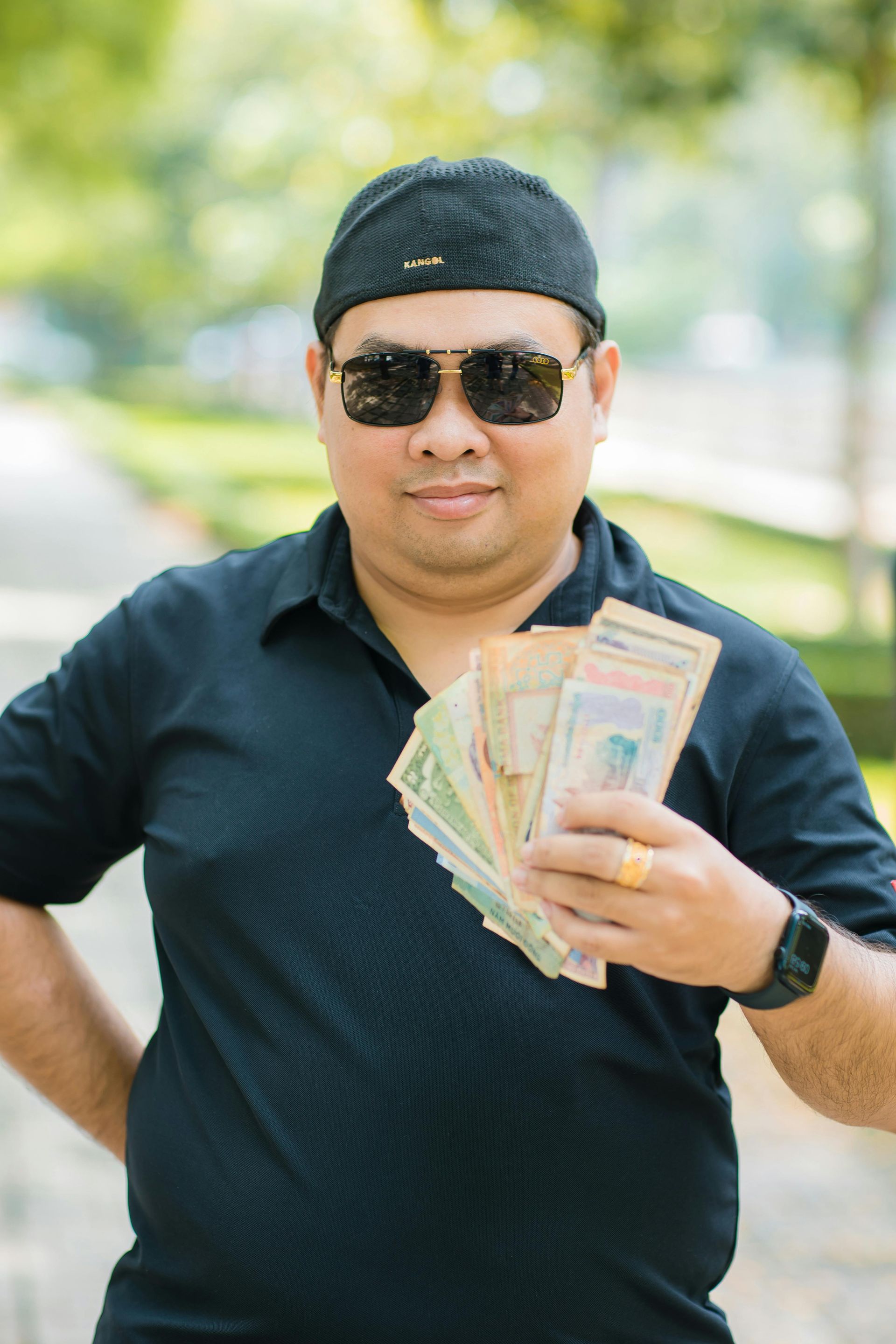 A man wearing sunglasses and a hat is holding a fan of money.