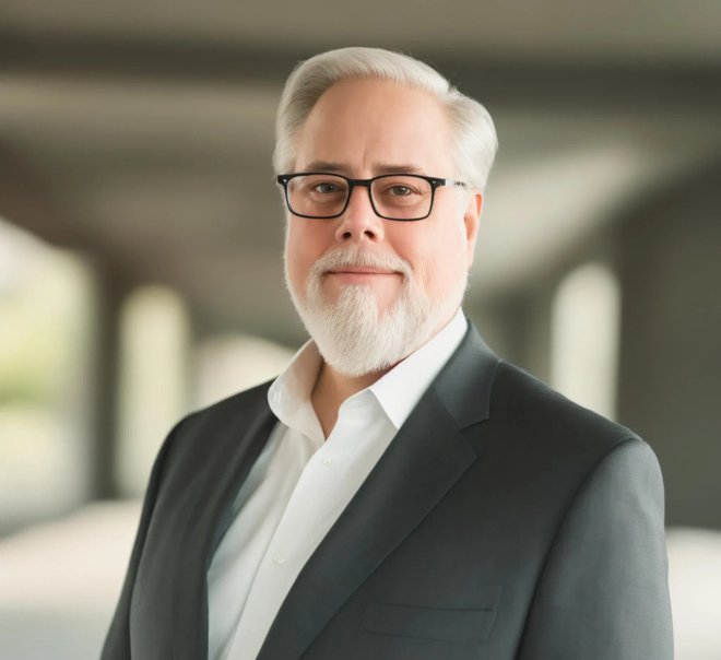 A man with a beard and glasses is wearing a suit and white shirt.