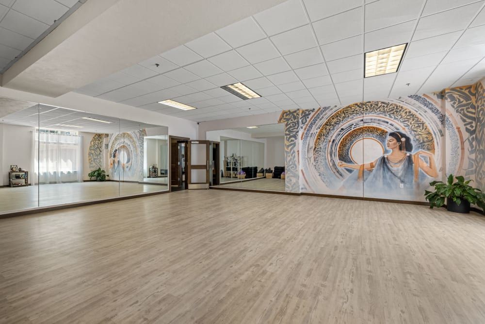Spacious dance studio with large mirrors and an artistic mural of a woman dancing with flowing drapery on the opposing wall, wooden flooring, and a door on the left leading out of the room at Copperline at Point Ruston in Tacoma, WA.