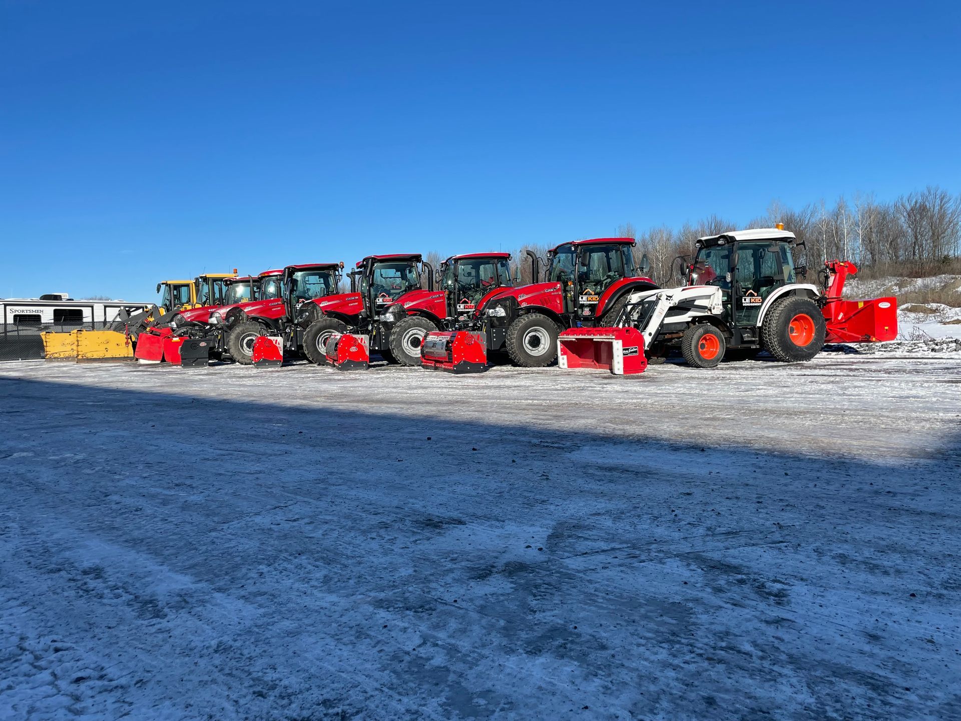 Une rangée de tracteurs rouges et blancs garés sur un terrain enneigé.