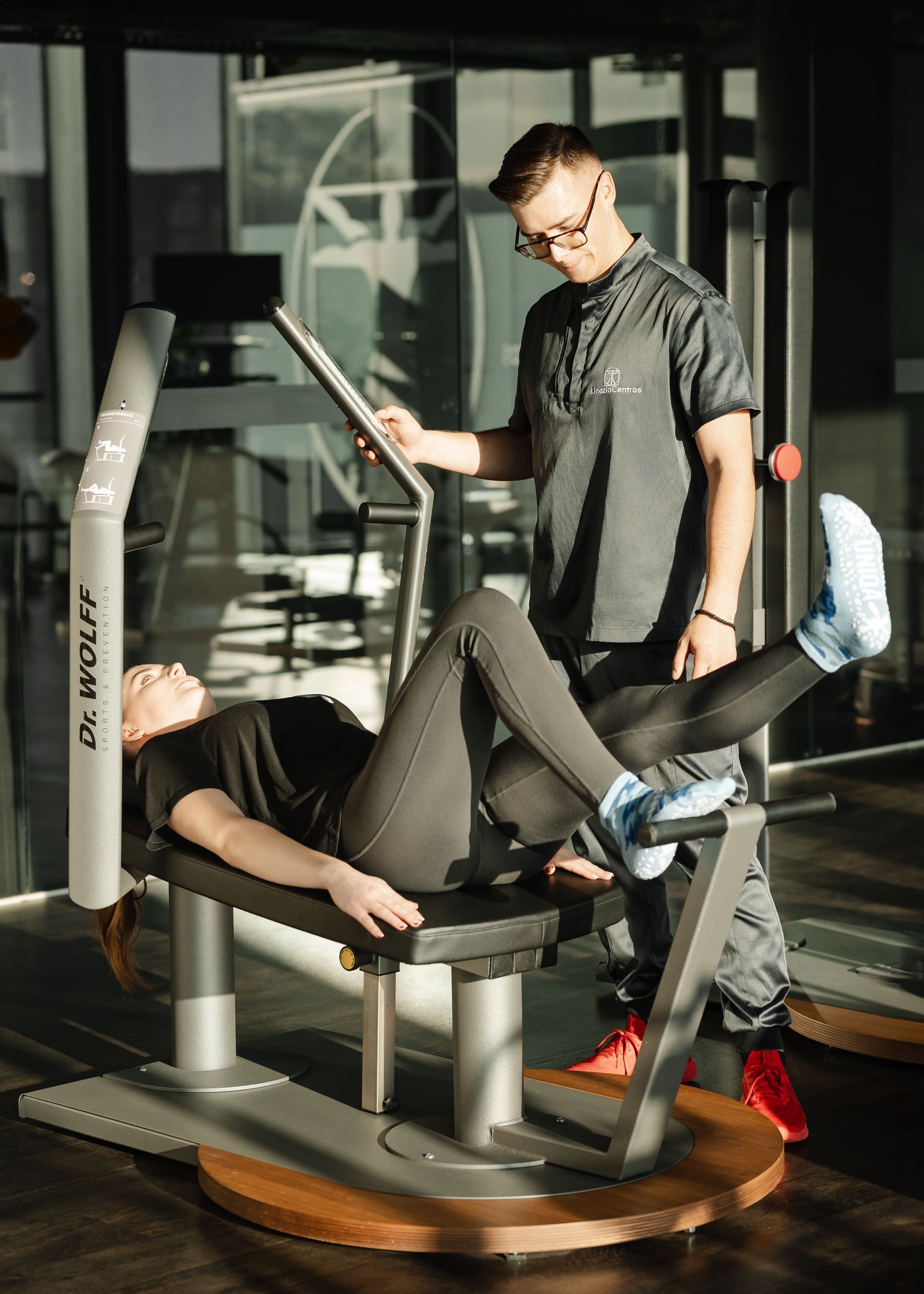 Vyras padeda moteriai atlikti pratimus ant treniruoklio sporto salėje.