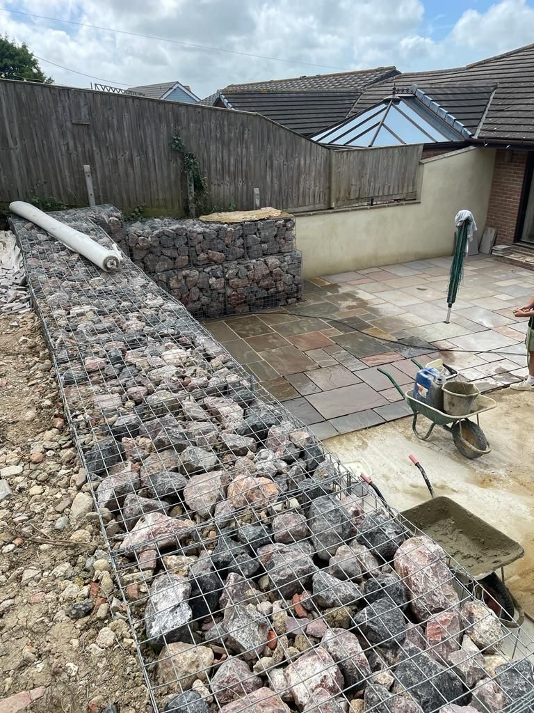 A wheelbarrow is sitting next to a pile of rocks in front of a house. 