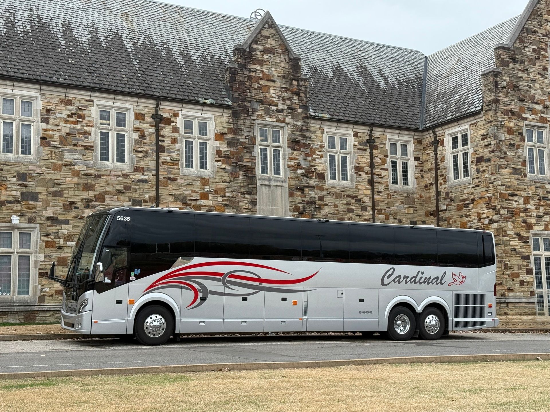 Charter bus parked in front of a stone academic building on a college campus.