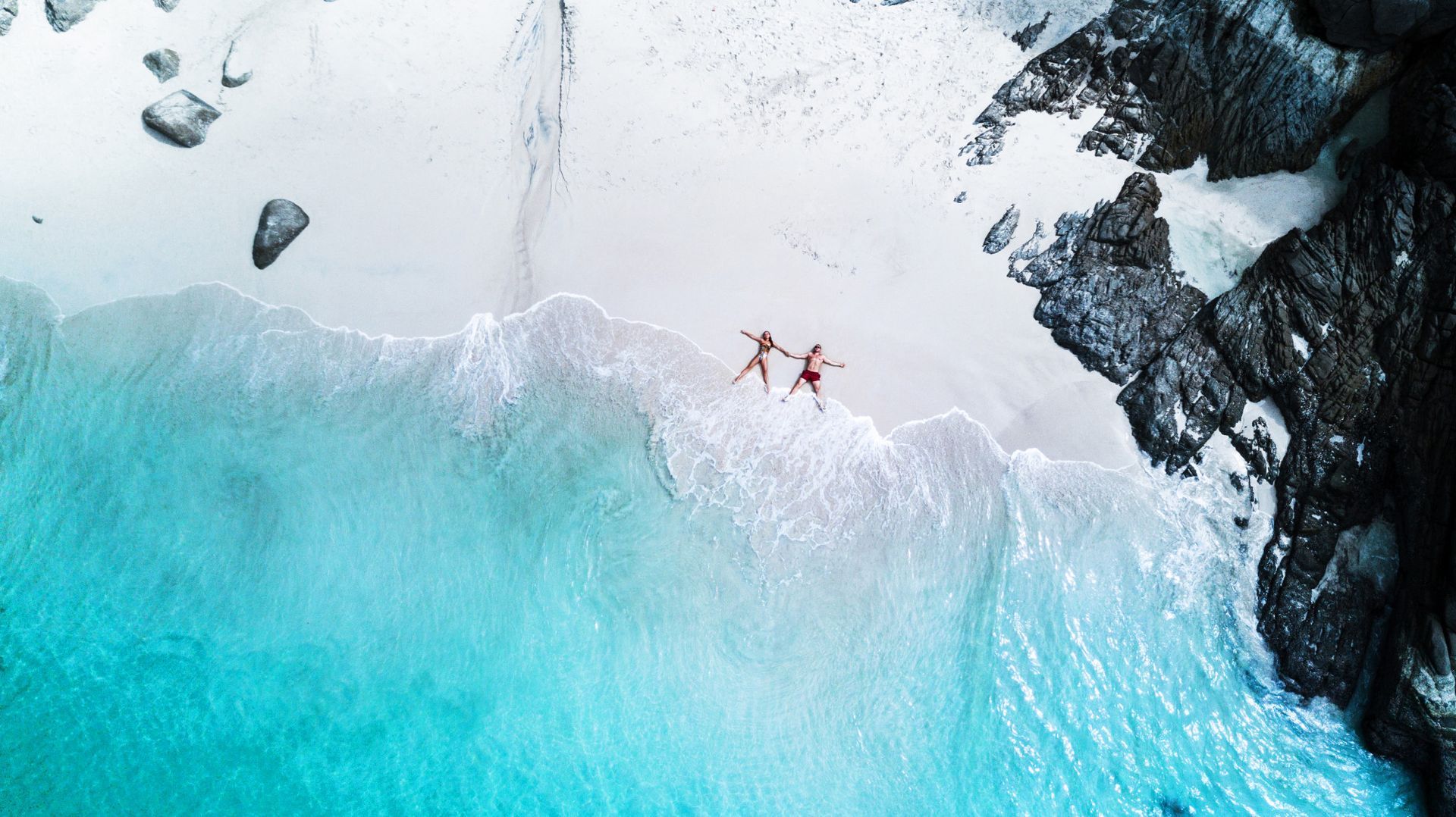An aerial view of a couple holding hands on a beach.