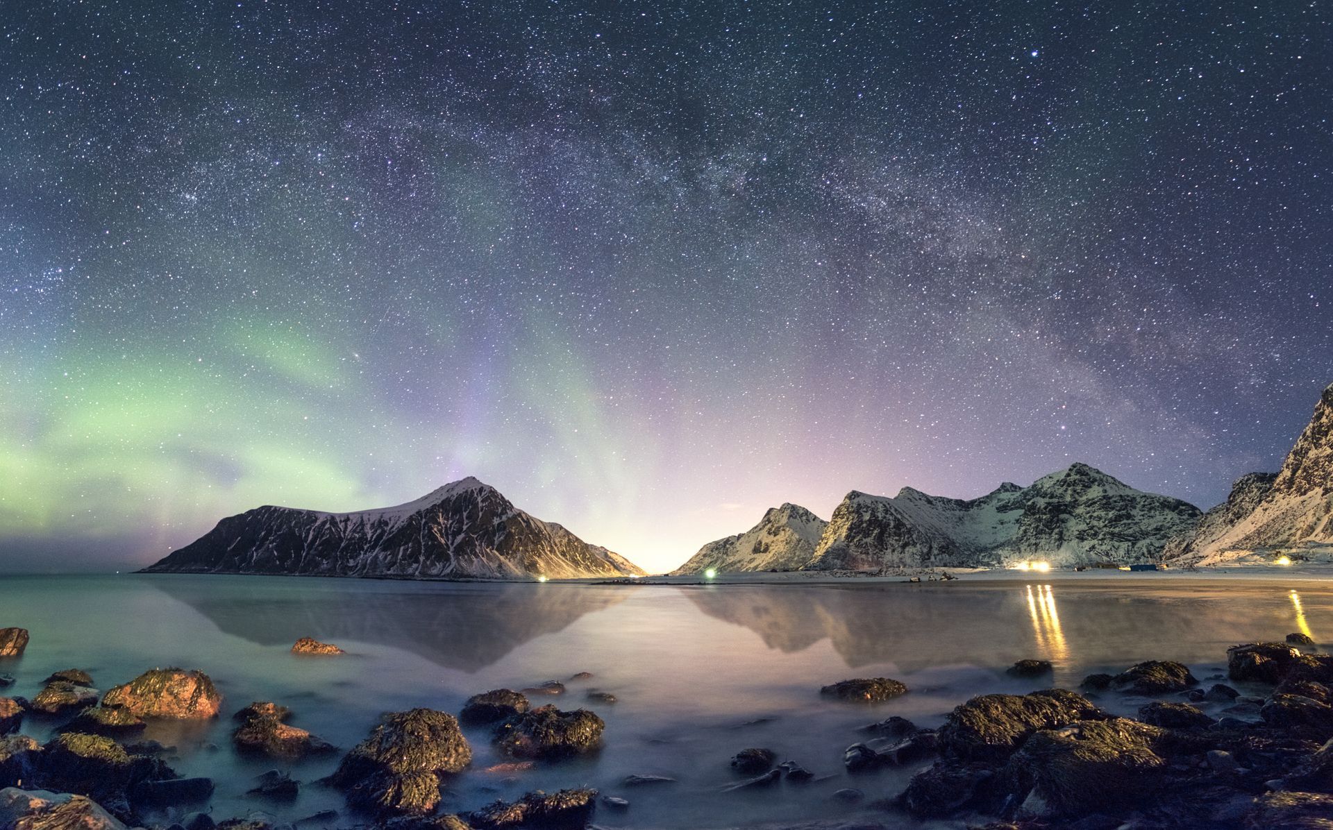 The aurora borealis is shining over a lake with mountains in the background