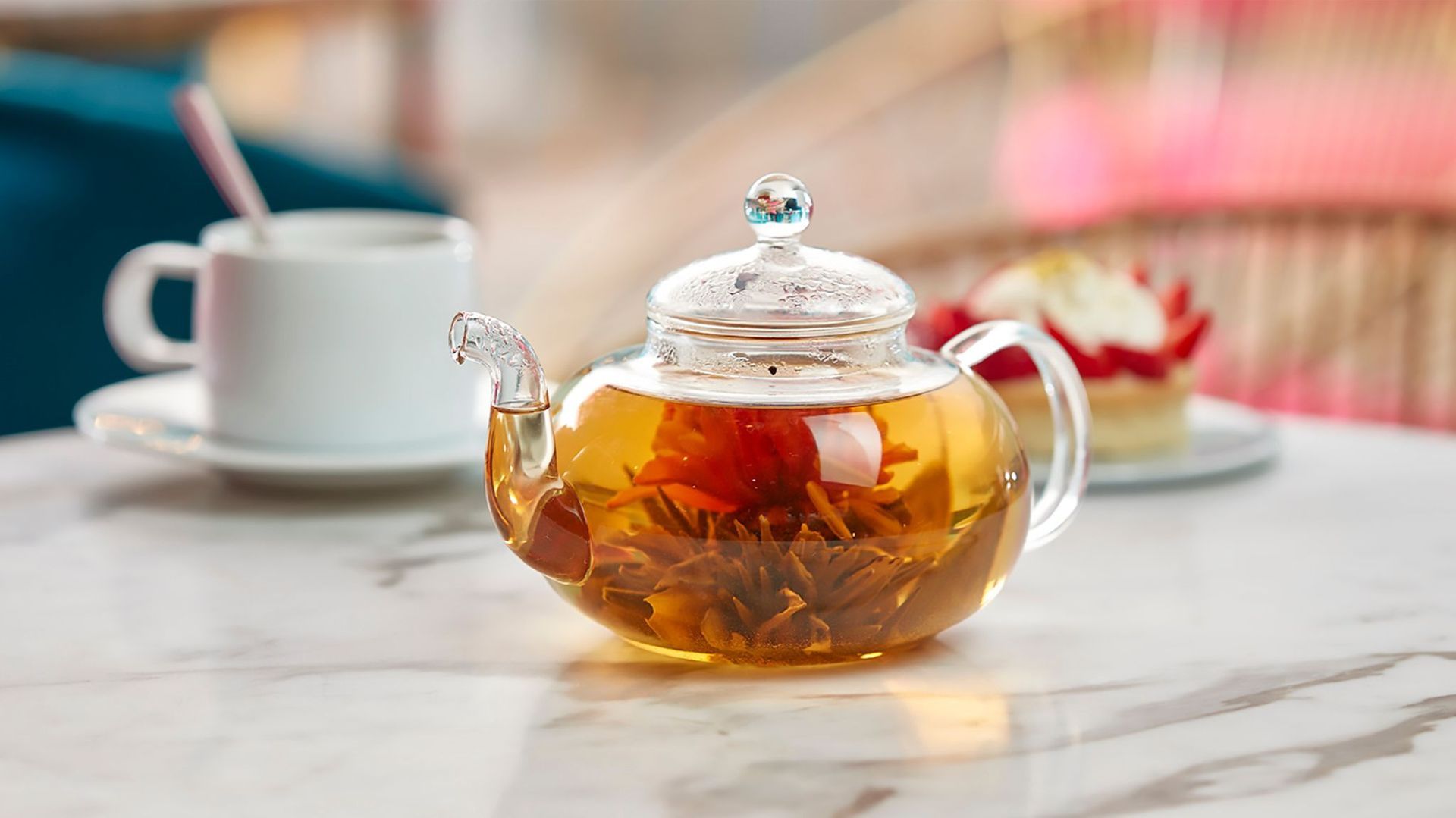 A glass teapot filled with tea is sitting on a table next to a cup of tea.