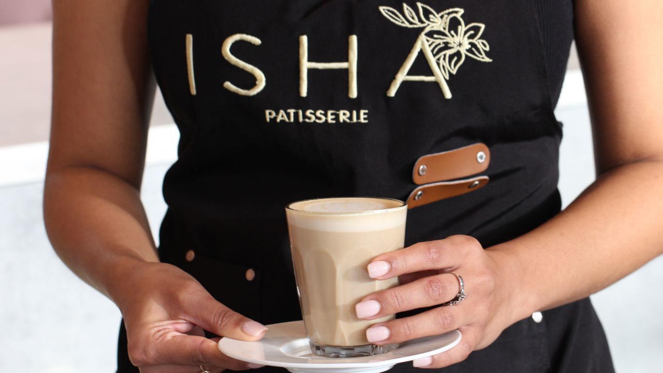 A woman in an apron is holding a cup of coffee on a saucer.