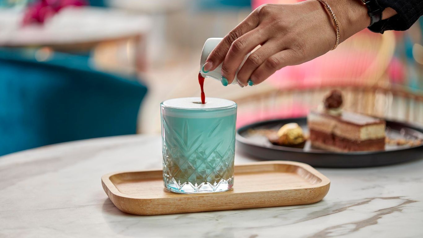 A person is pouring a drink into a glass on a table.