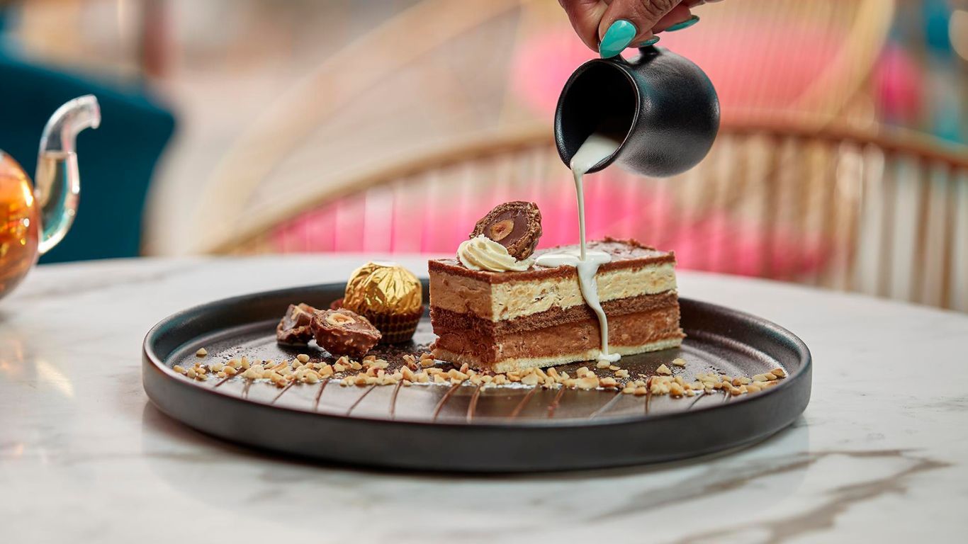 A person is pouring milk on a piece of cake on a plate.