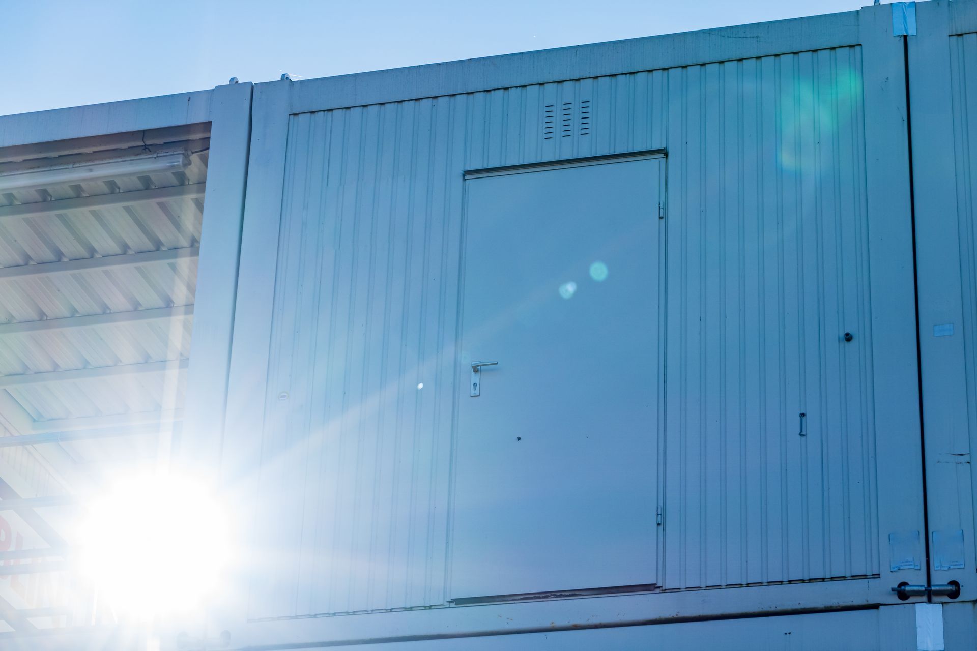 White mobile storage container with a secured door, placed outdoors in bright daylight.