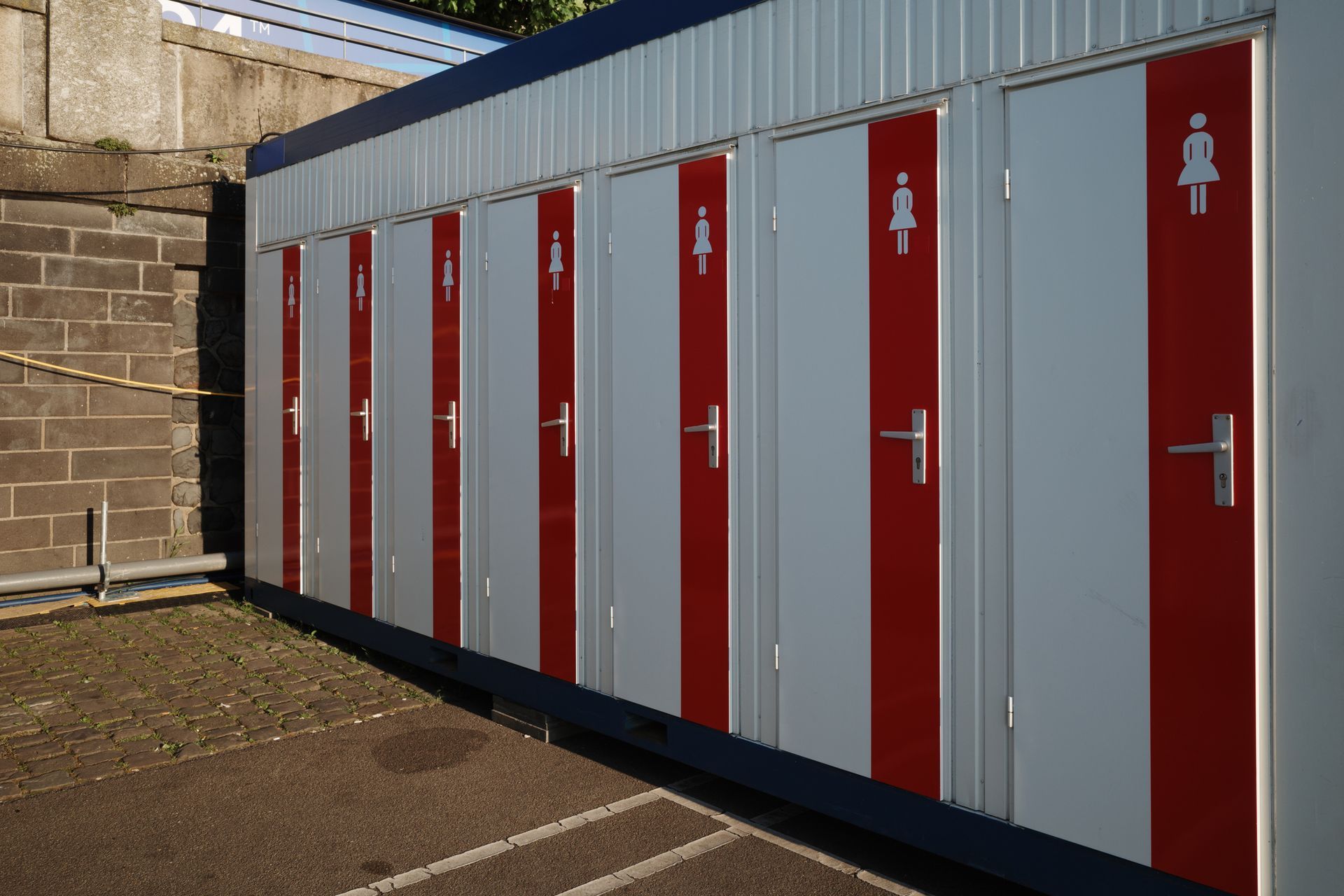Portable toilets built into mobile storage containers for rent with red and white doors.