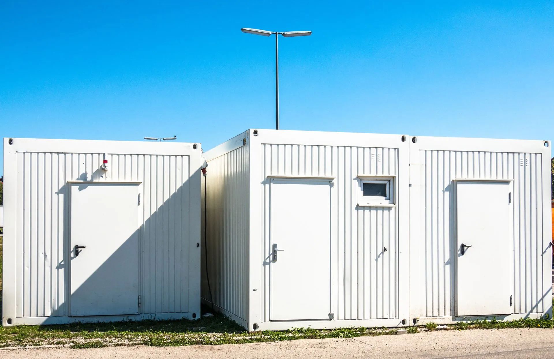 Three white modular storage containers or portable office units standing side-by-side under a clear blue sky.