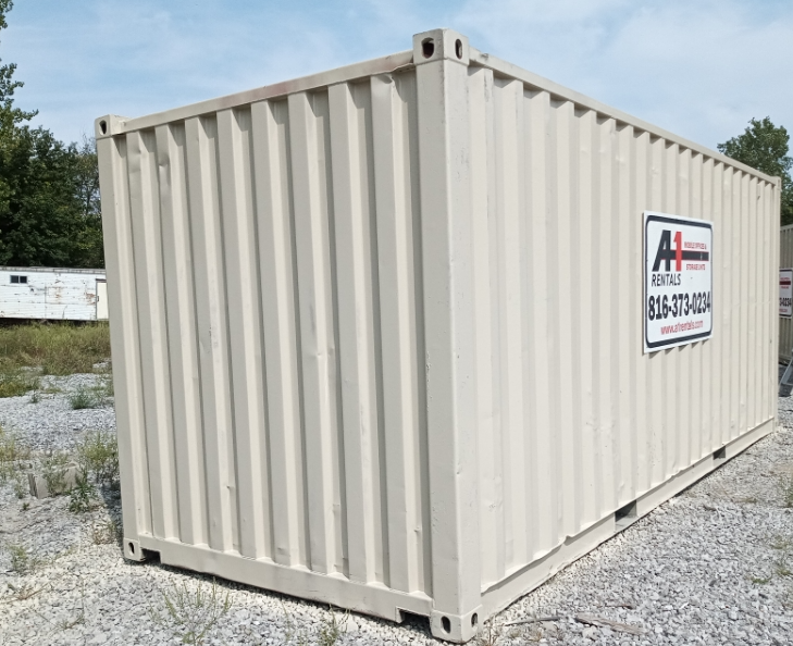 A tan corrugated steel shipping container sits on a gravel lot under a bright sky