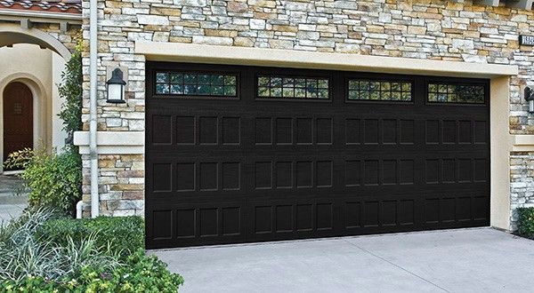 A large black garage door is sitting in front of a stone building.