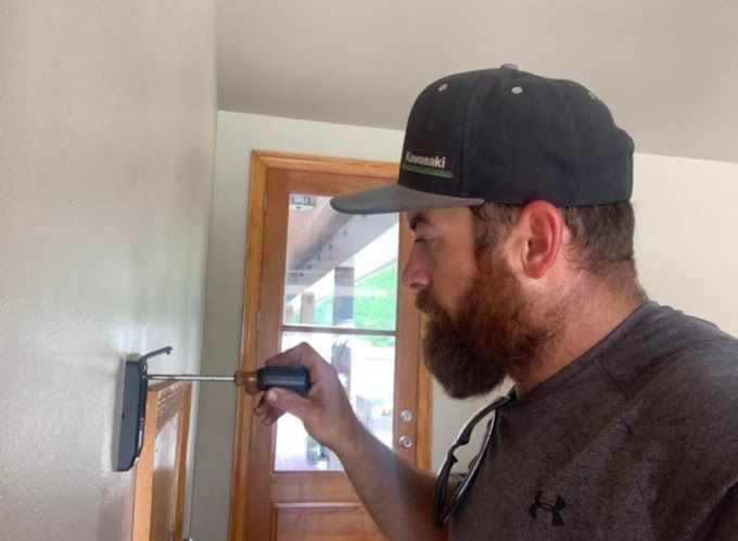 A man with a beard is using a screwdriver on a wall.