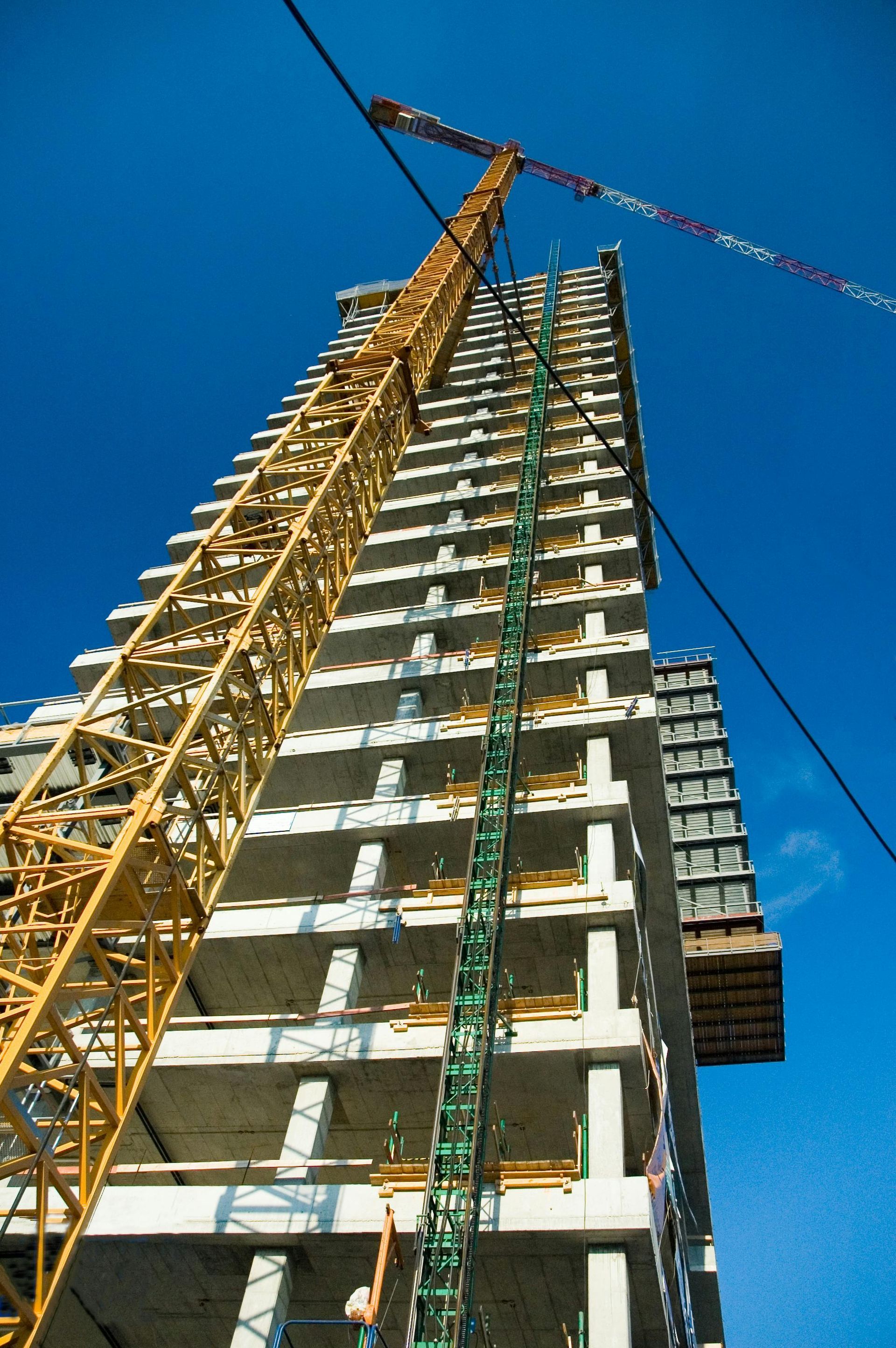Construction crane next to a tall building under construction against a bright blue sky.