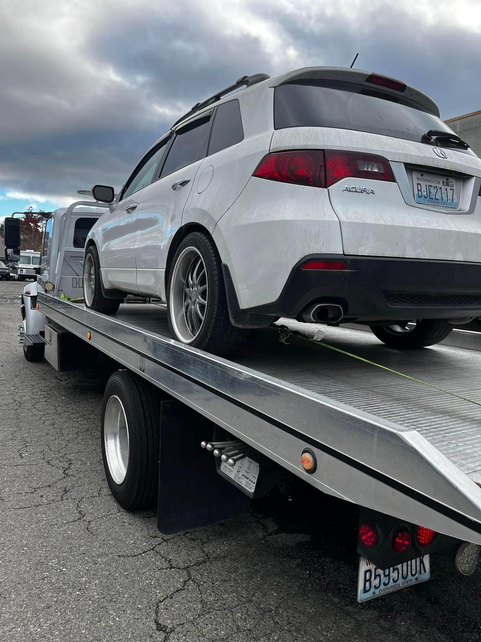 A white SUV parked on the flatbed of a tow truck outdoors under a cloudy sky.