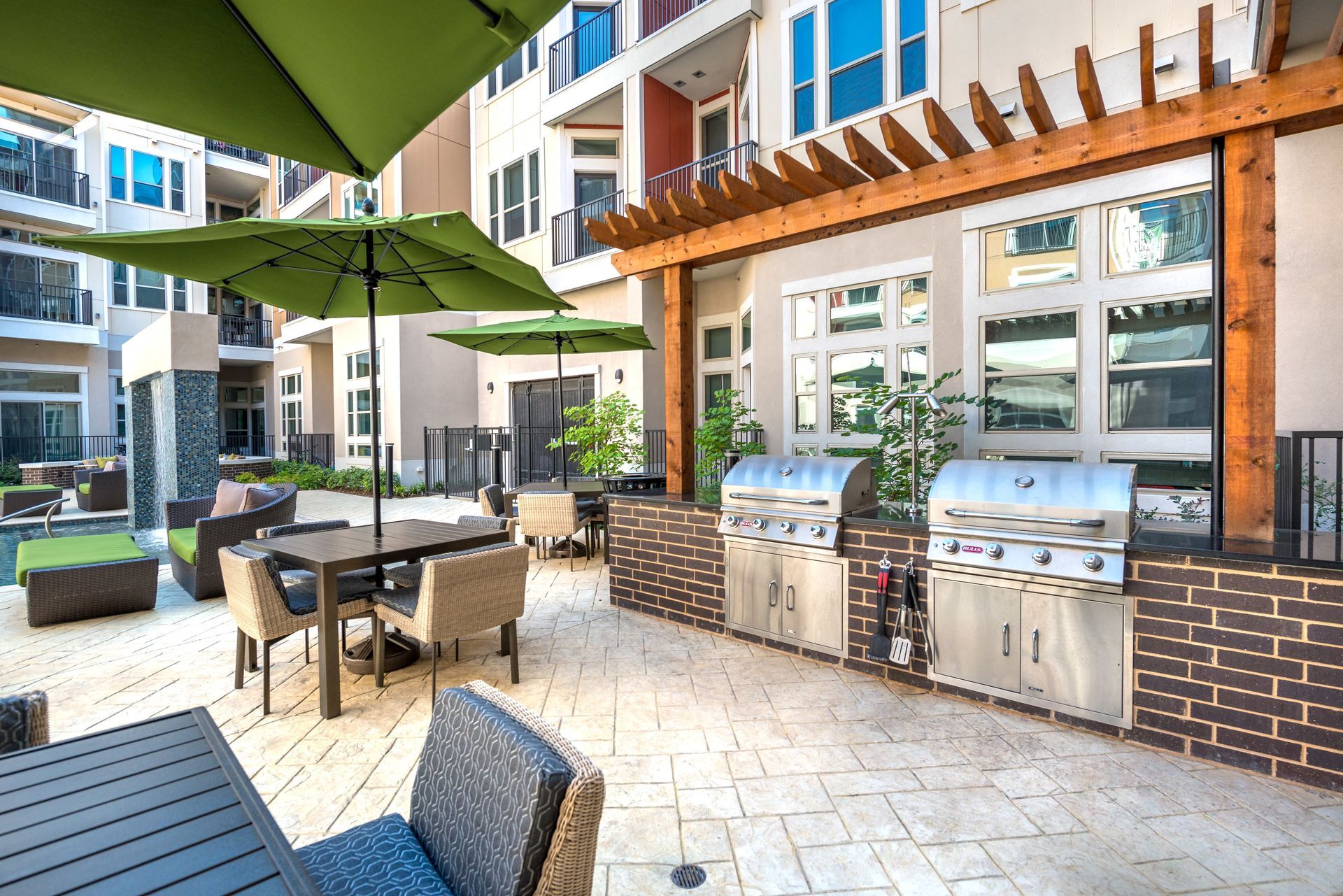 A patio with tables, chairs, umbrellas, and a grill.