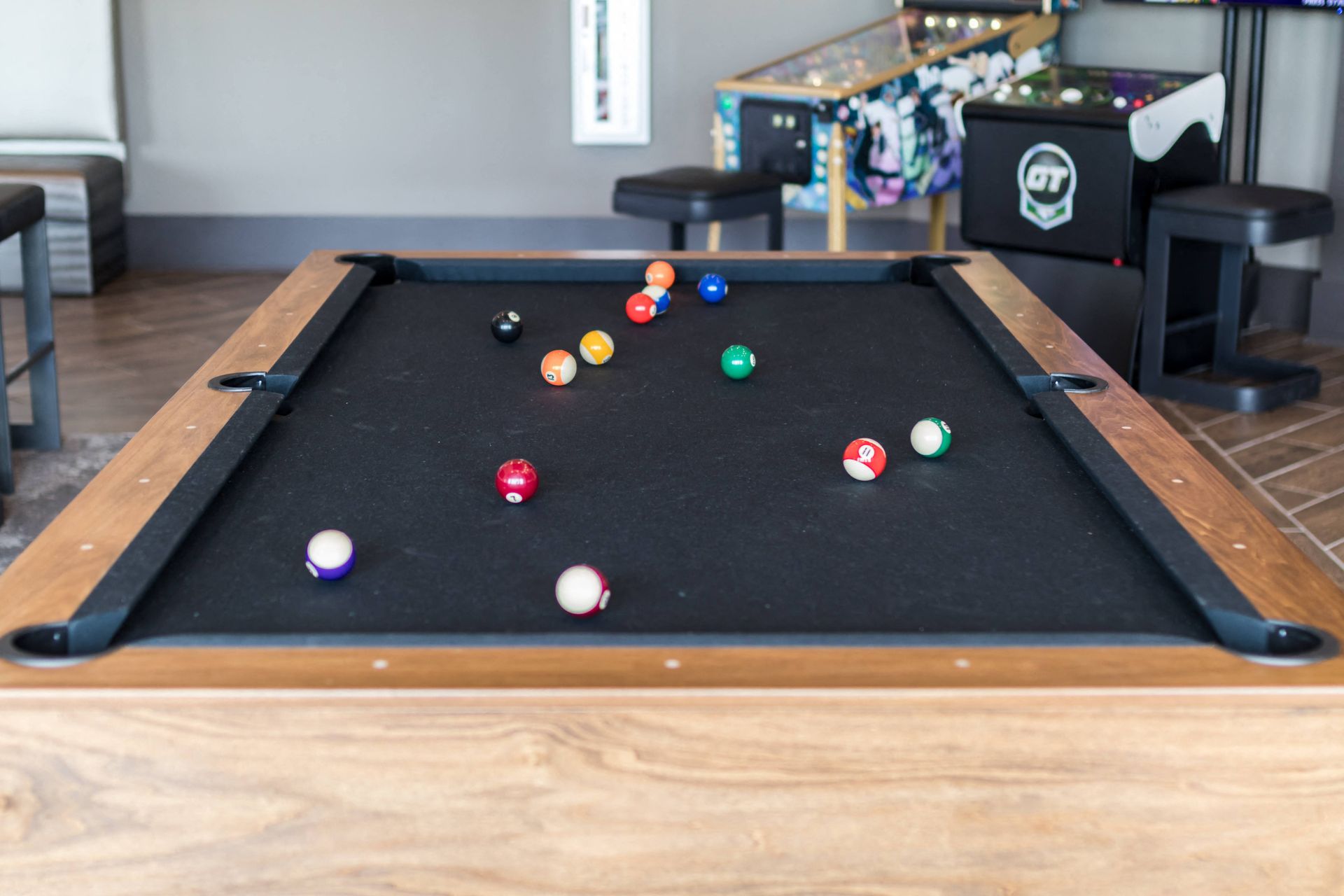 A pool table with balls on it and a pinball machine in the background.