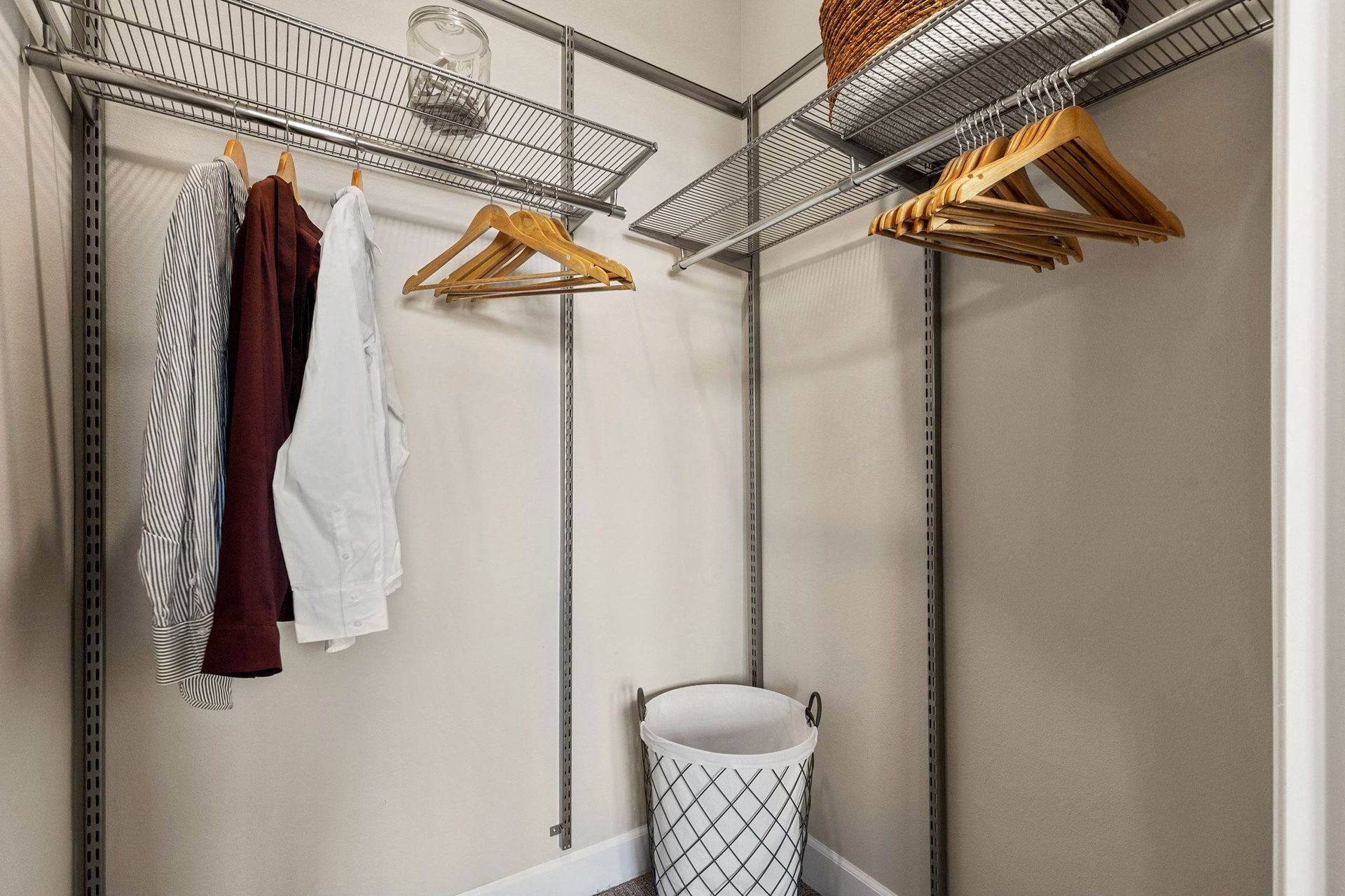 A walk in closet with clothes hanging on racks and a laundry basket.