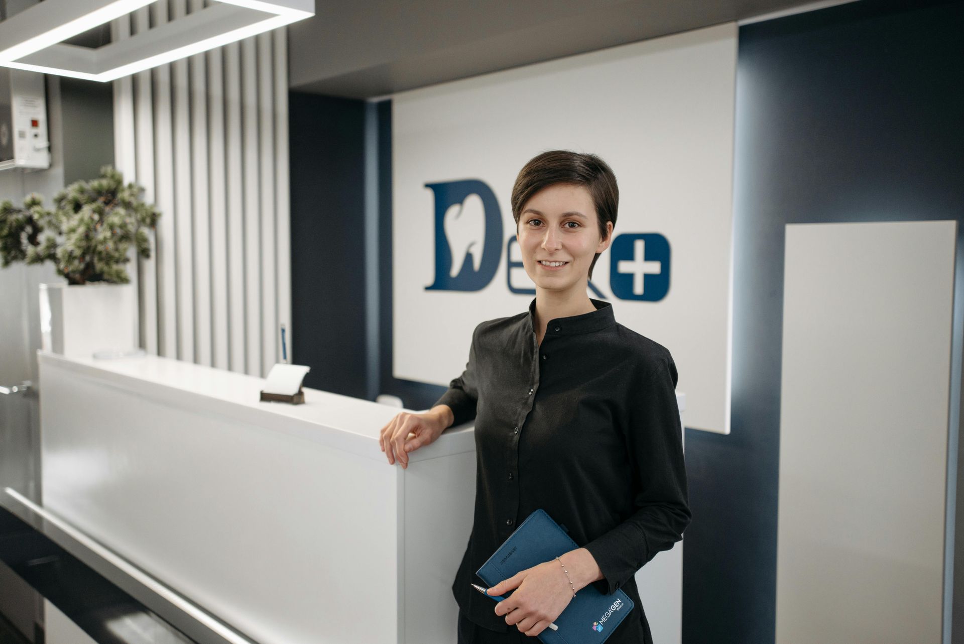 A woman is standing in front of a reception desk in a dental office.