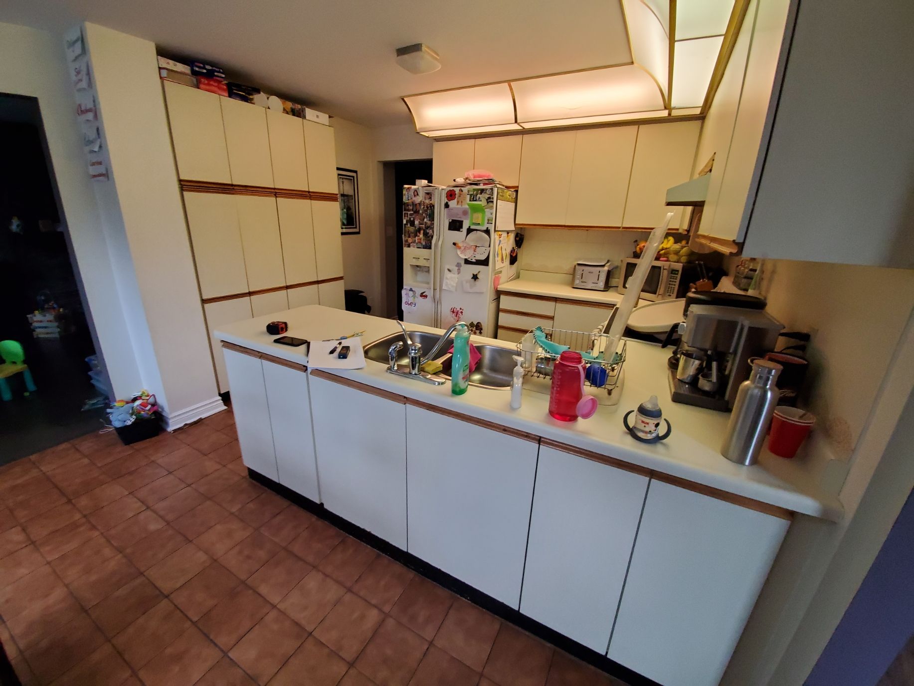 A kitchen with white cabinets , a refrigerator , a sink , and a coffee maker.